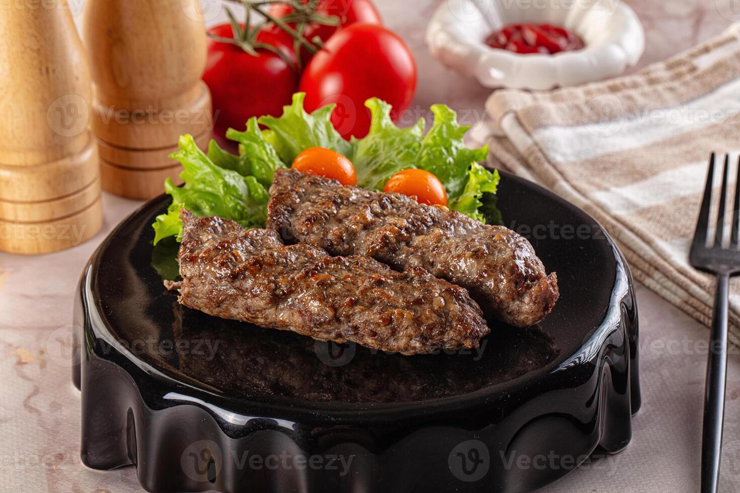 Two pieces of meat on a black plate with lettuce and tomatoes photo
