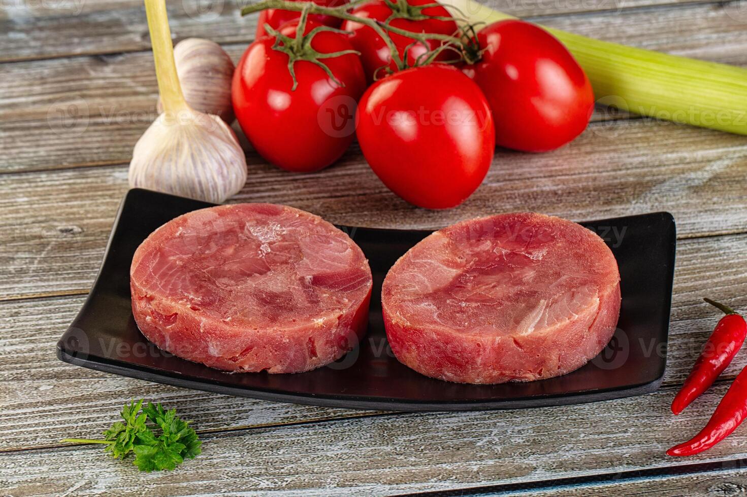 Two raw meat patties on a black plate with vegetables photo
