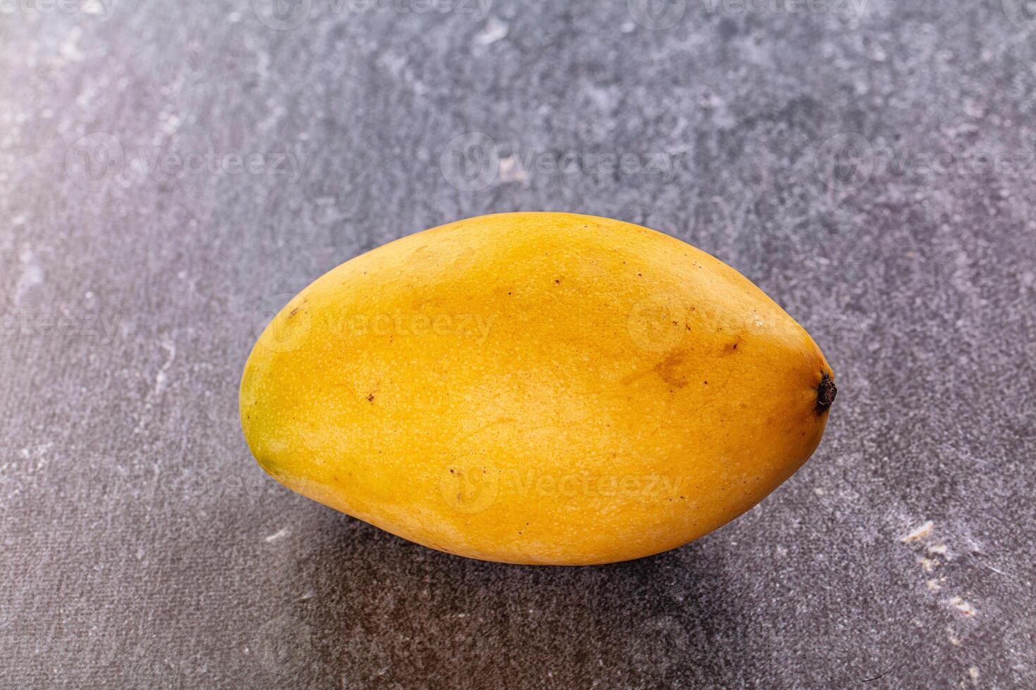 A single yellow mango on a gray surface photo