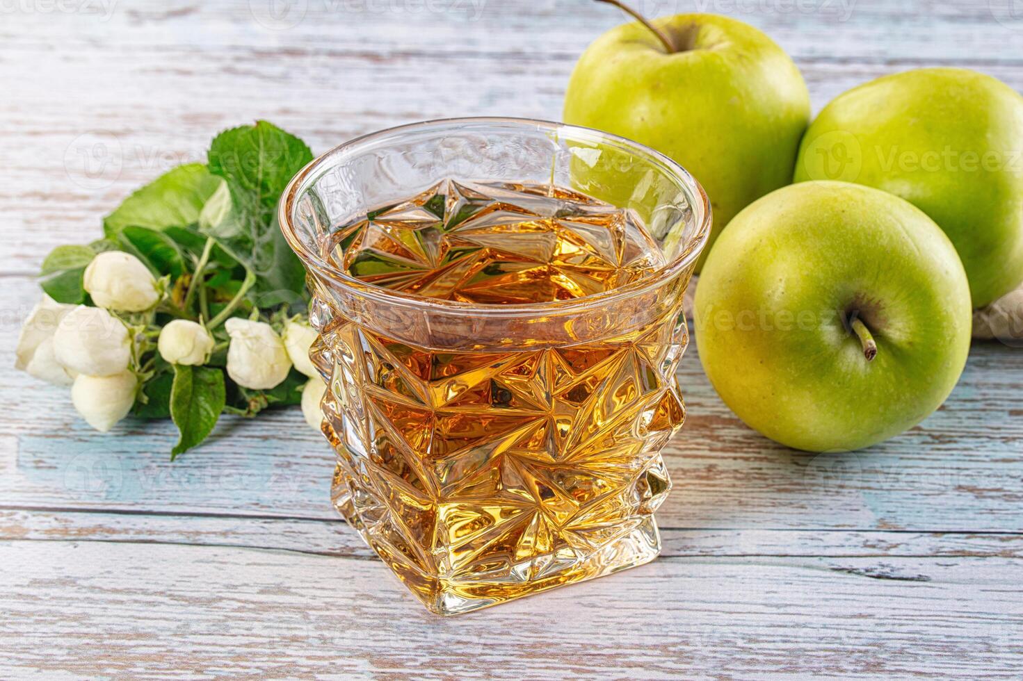 A glass of apple juice next to a bowl of apples photo