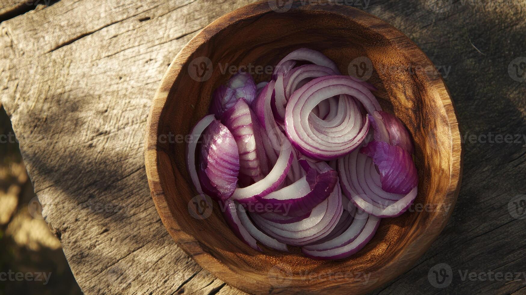 Thinly sliced red onions in a wooden bowl on a rustic wooden surface photo