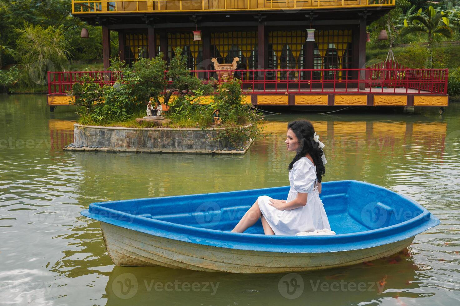 A young female traveler is sailing on a wooden boat on a lake against the background of a Buddhist temple standing on the water photo