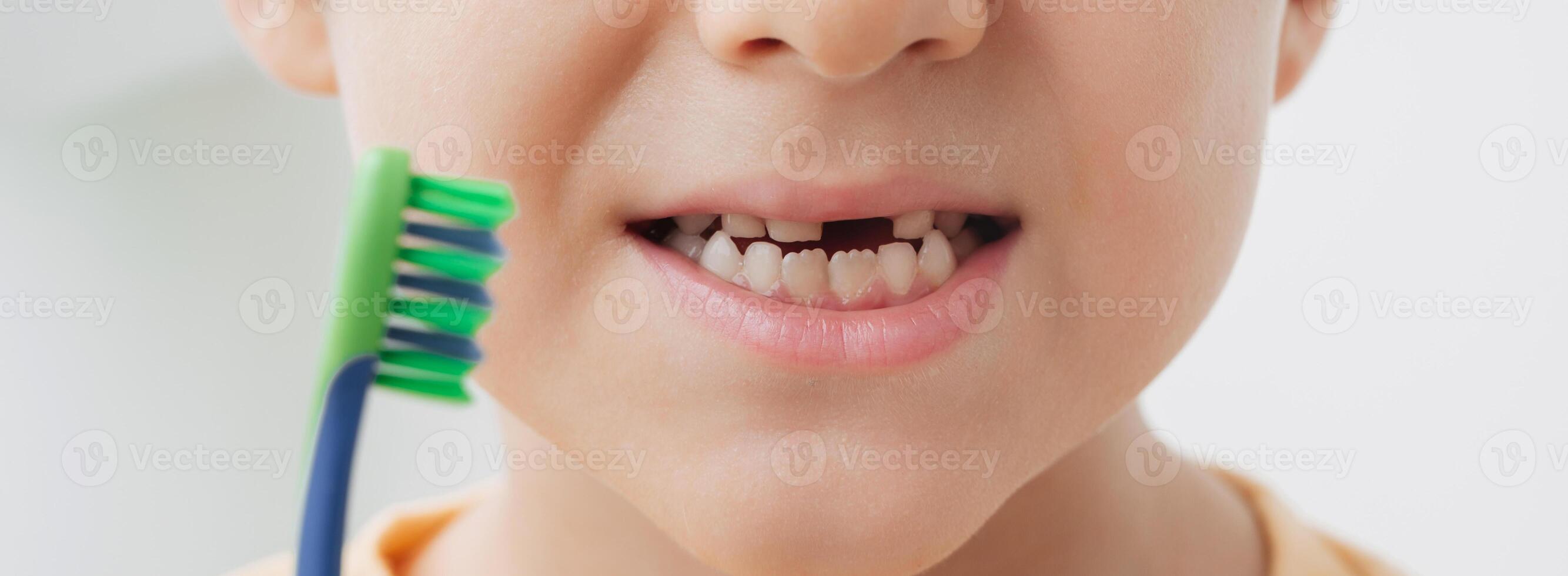 The smile of a little boy, without a baby tooth with a toothbrush, close-up. Panoramic banner. photo