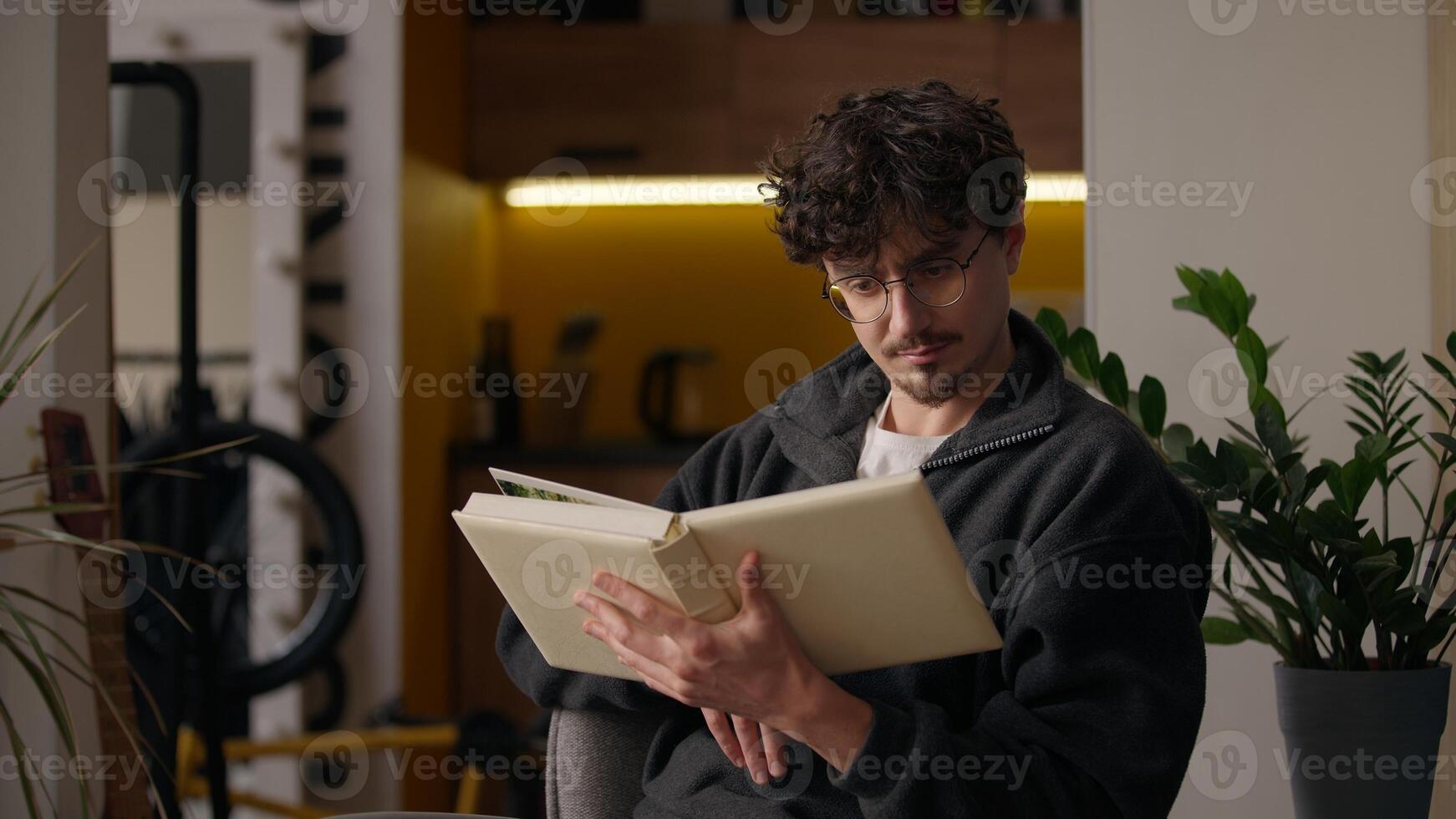 Concentrated Hispanic guy reading literature holding book at home hipster turning page focused smart adult man reader male looking text poetry relaxing enjoying novel hobby read story library leisure photo