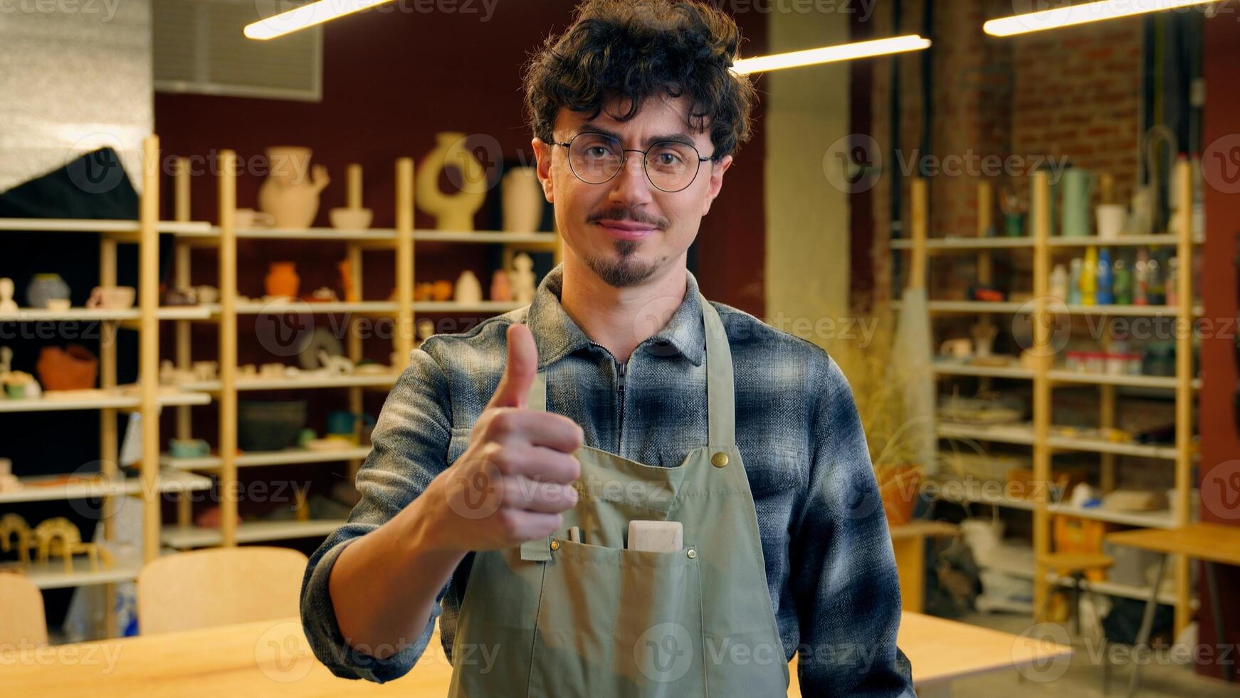 A man in an apron is giving a thumbs up in a pottery studio setting photo