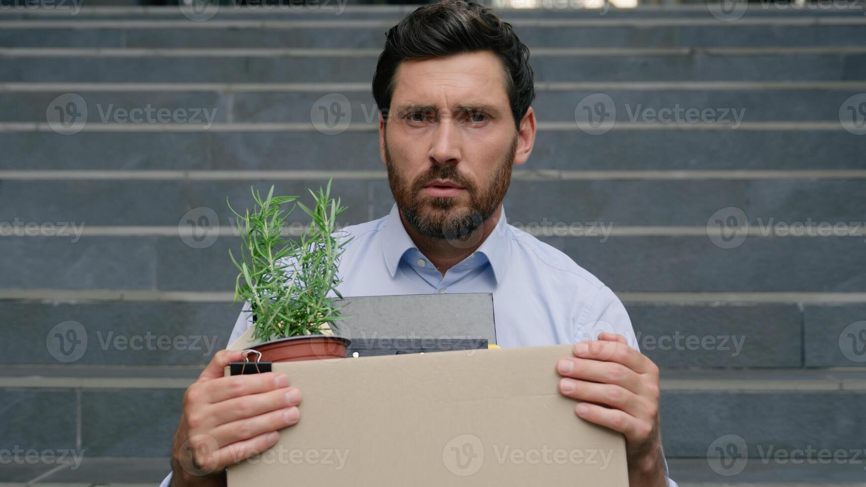 Upset unemployed fired Caucasian middle aged business man lost job looking at camera sad holding dismissal box sitting stairs near office building dismiss businessman male unemployment finance crisis photo