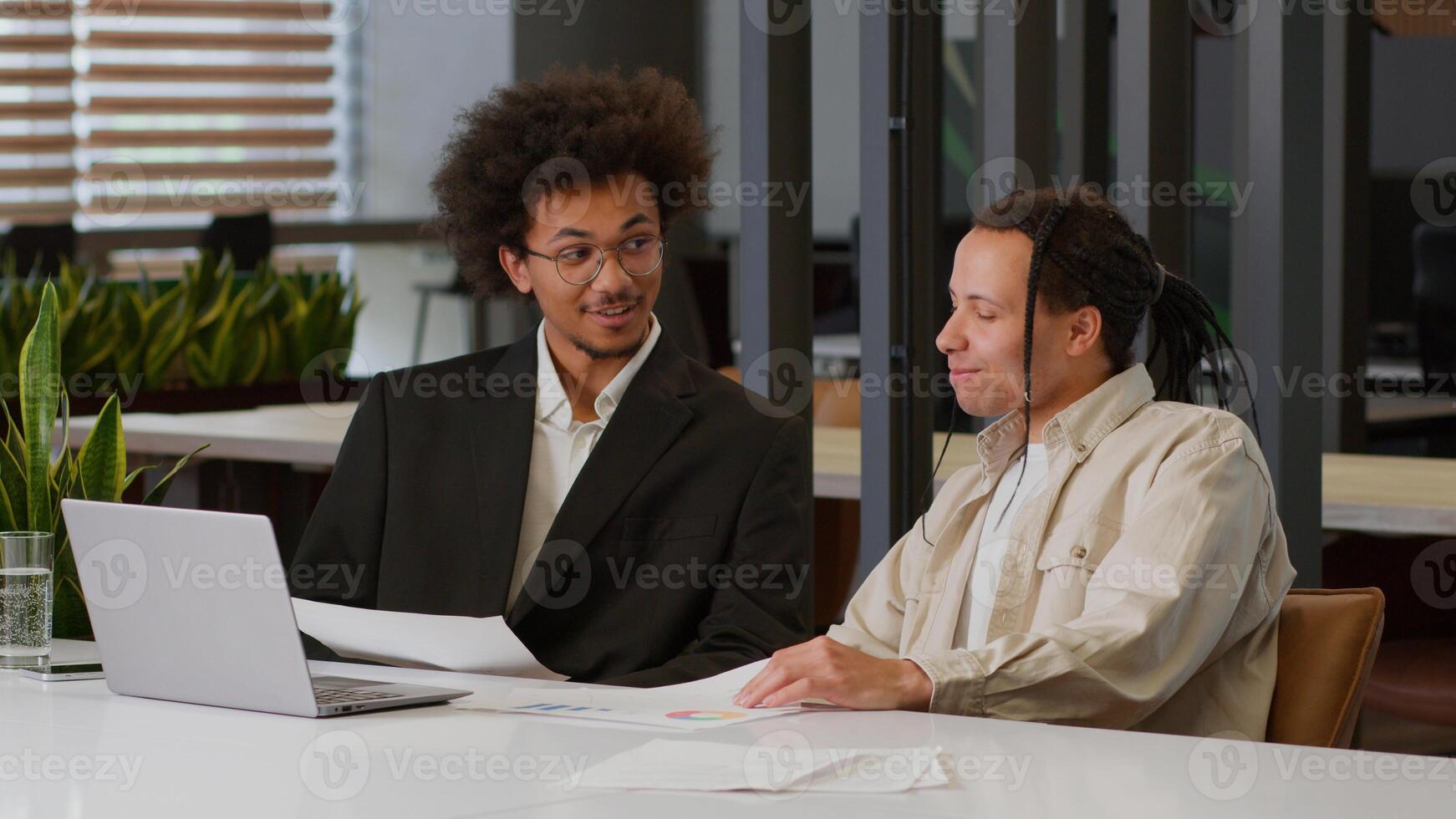 Two multiracial business men African American businessmen partners diverse colleagues males discuss online internet data analyzing marketing project result using laptop talk at office desk cooperation photo