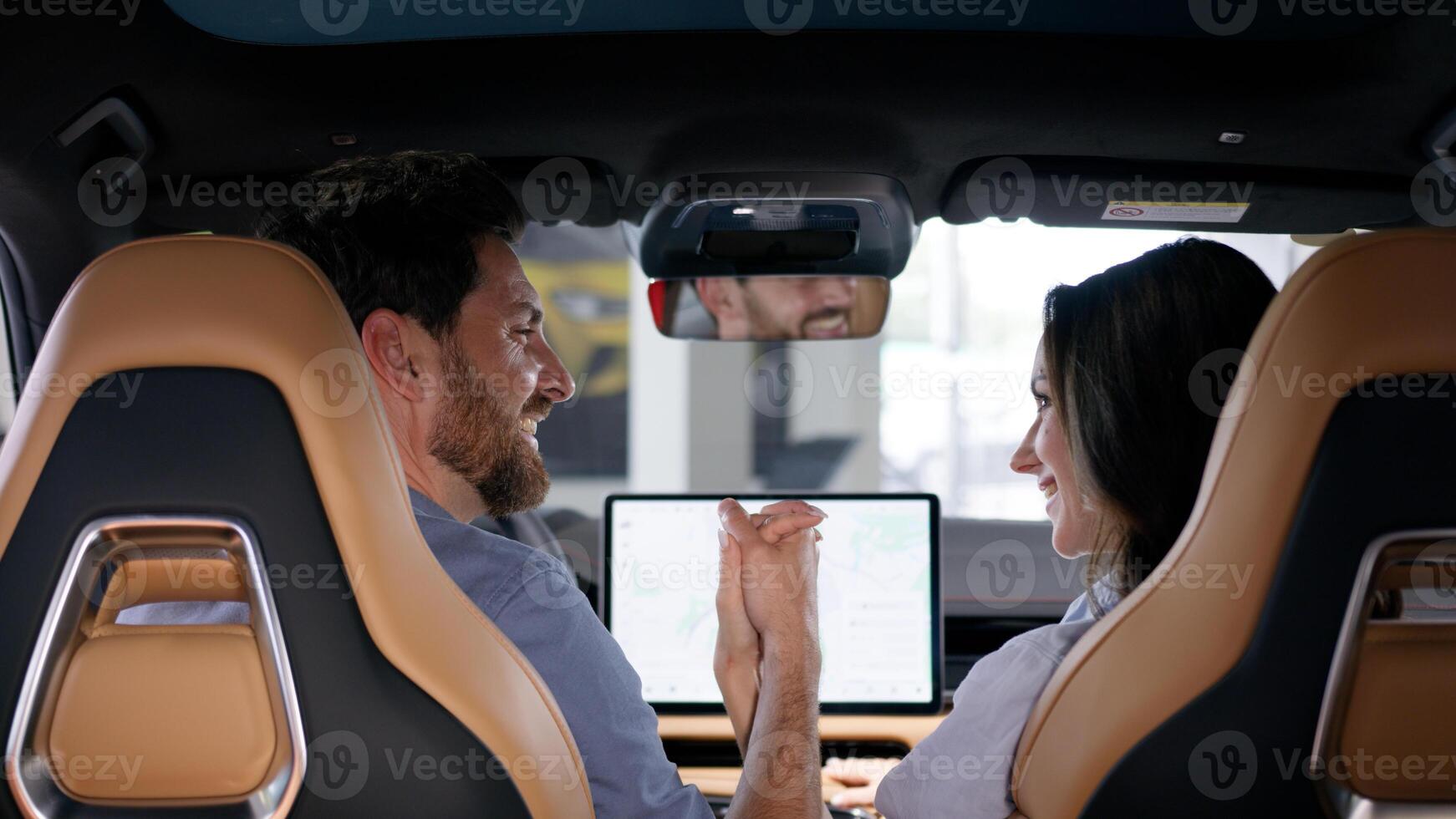 Back view happy family Caucasian couple inside automobile buying auto smiling looking in each other holding hands bonding travel man guy male boyfriend husband in car woman girl female girlfriend wife photo