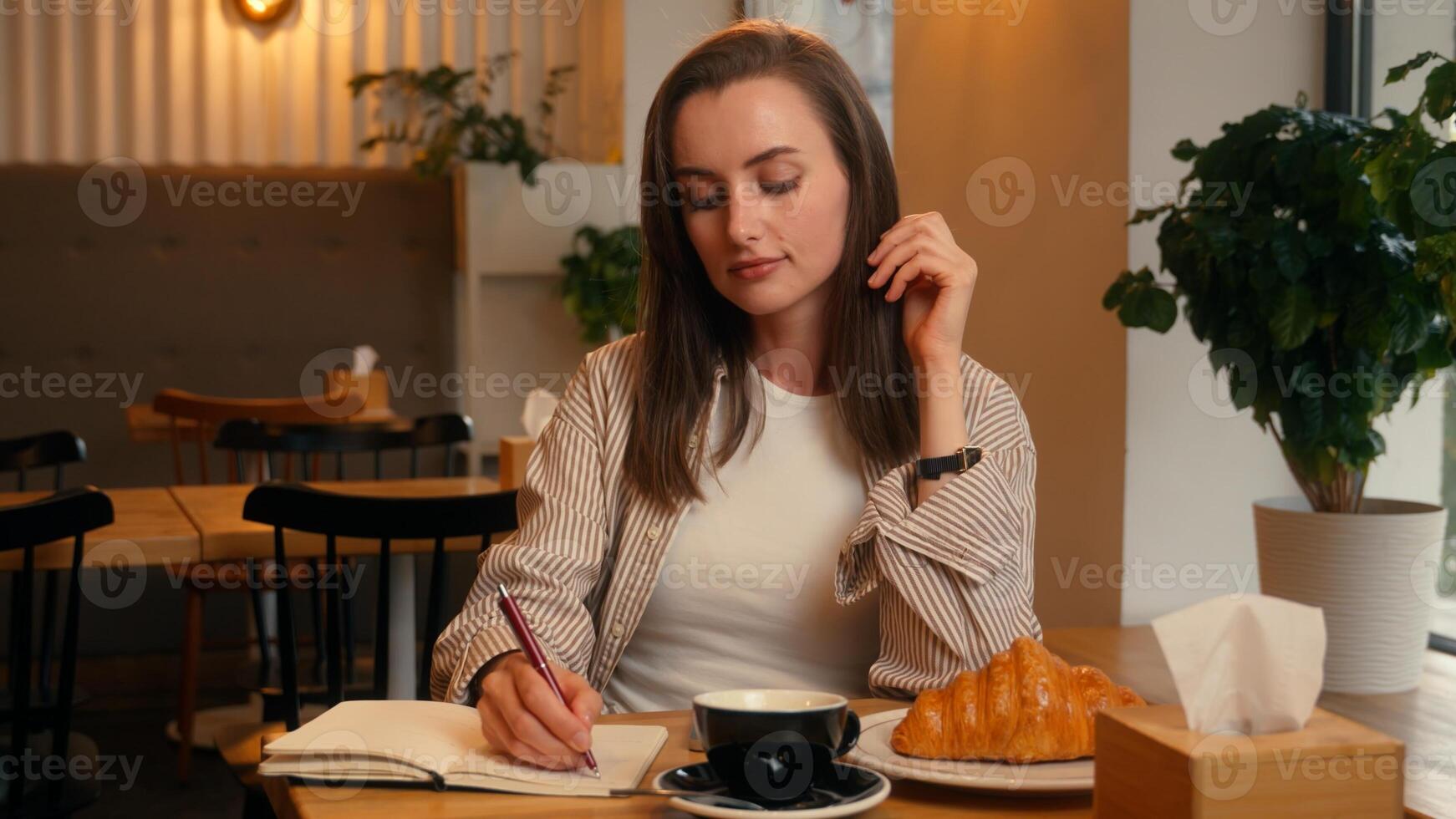 Caucasian woman in cafe inspired writing notes in notebook drinking coffee lunch happy female girl at cafeteria table drink tea with croissant write diary information noting idea handwriting plan photo