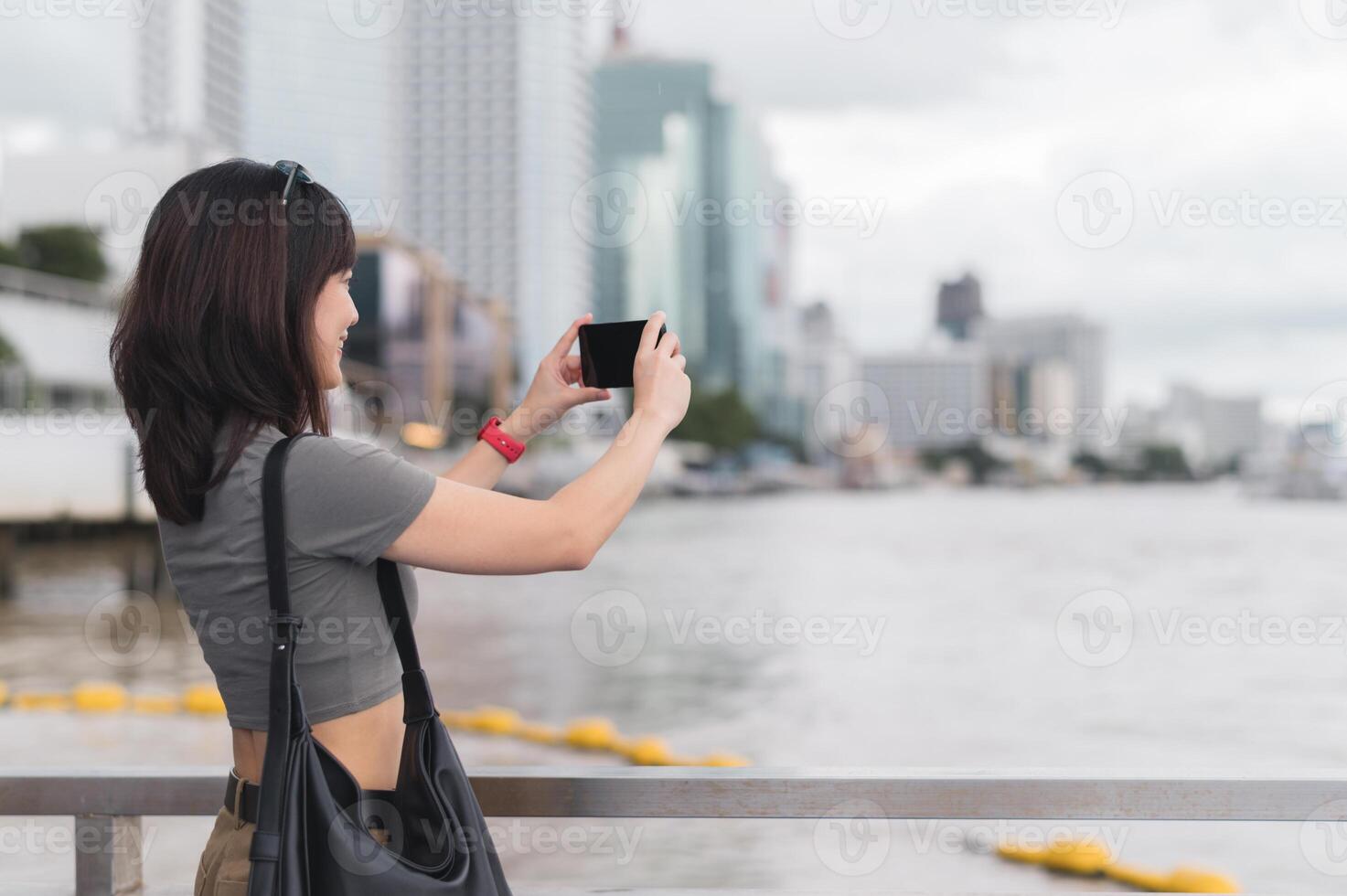 Solo southeast asian woman teenager blogger world travel tourism experience Bangkok Thailand. She wait for boat Chao Phraya river and take photo with smartphone to express local cultural concept