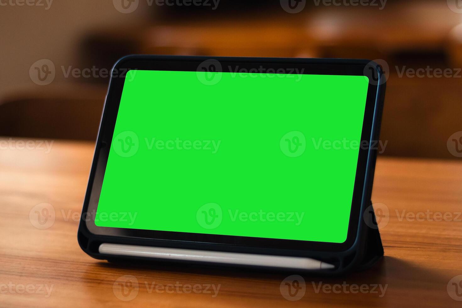 A side view of a tablet device with a blank green screen on the table photo