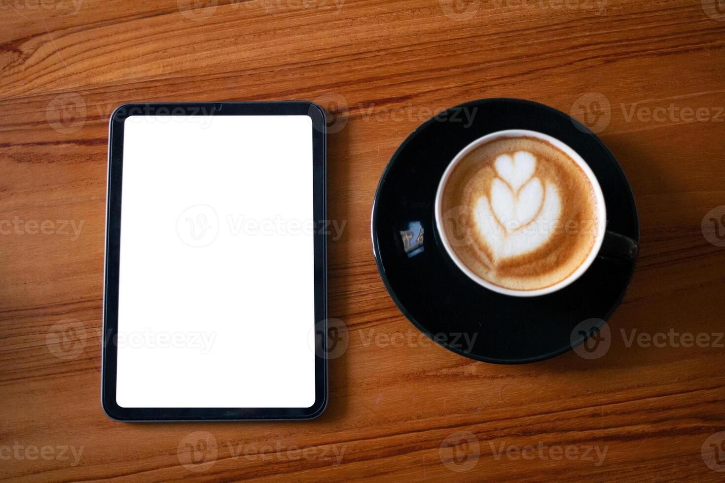 Tablet with blank white screen display beside a black cup of cappuccino on natural wood. photo