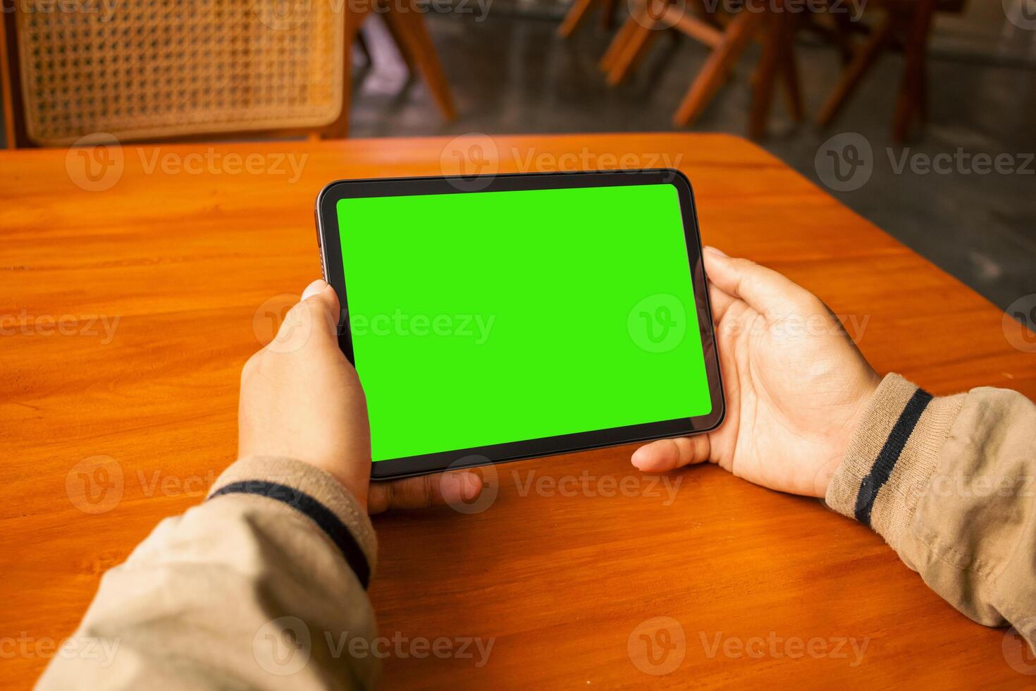Man viewing a tablet with a blank green screen in a cozy cafe setting photo