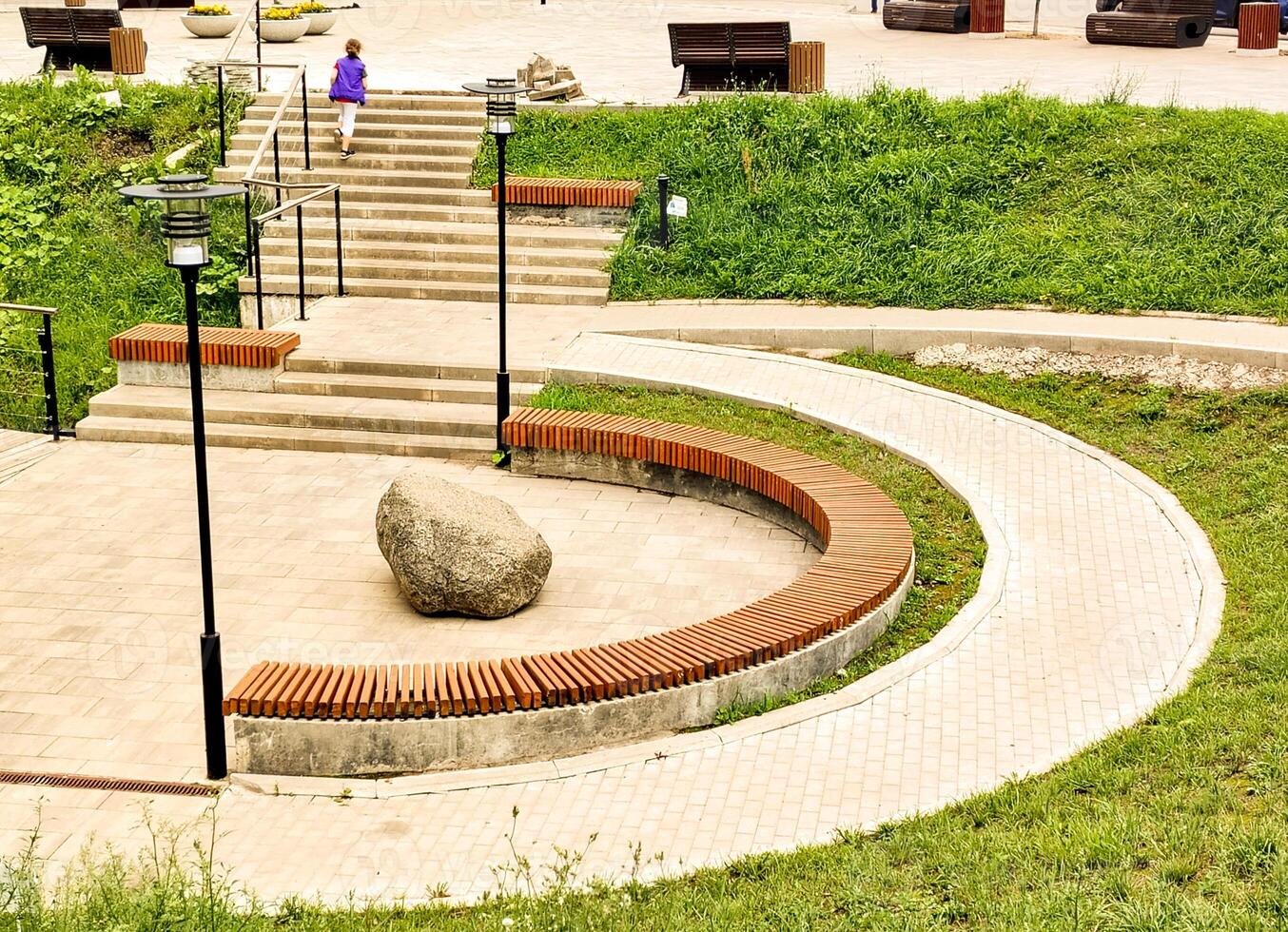 Close-up of a wooden bench and an arc-shaped sidewalk in a city park on a sunny summer day. photo