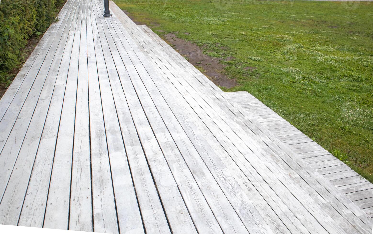 Natural sidewalk made of light wood planks, against the grass in the park photo