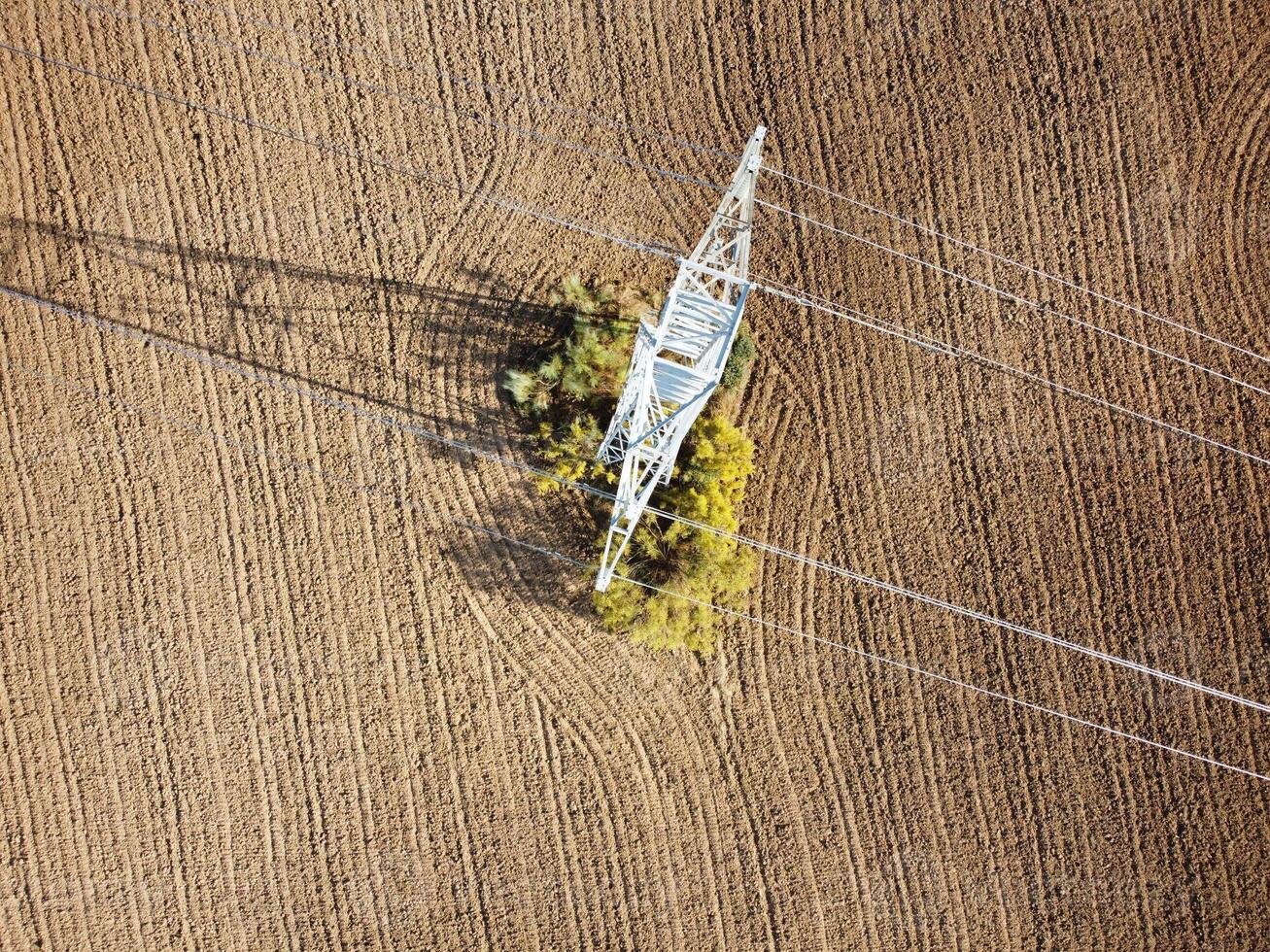 Power lines intersect with a field surrounded by autumn foliage in a rural landscape during midday photo