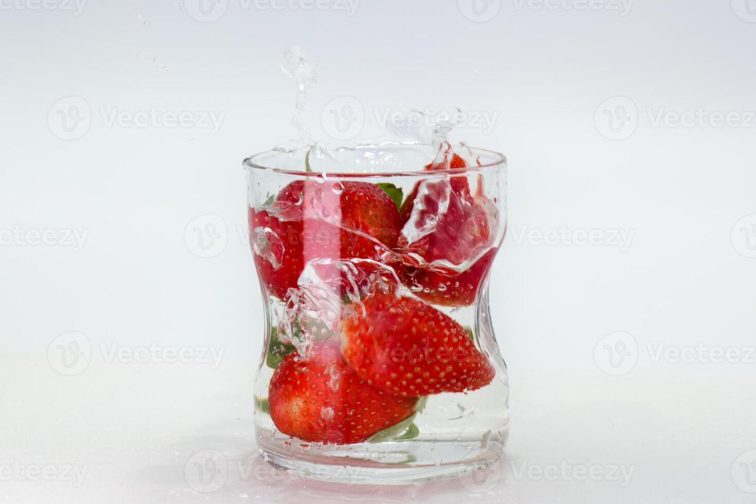 Fresh strawberries create a splash in a glass of water, showcasing vibrant colors and textures in a playful moment photo
