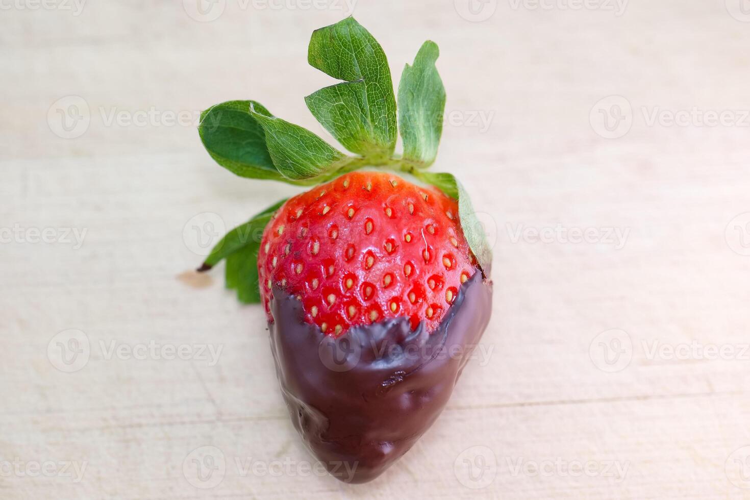 Delicious chocolate dipped strawberry resting on a wooden surface, showcasing vibrant red color and fresh green leaves photo