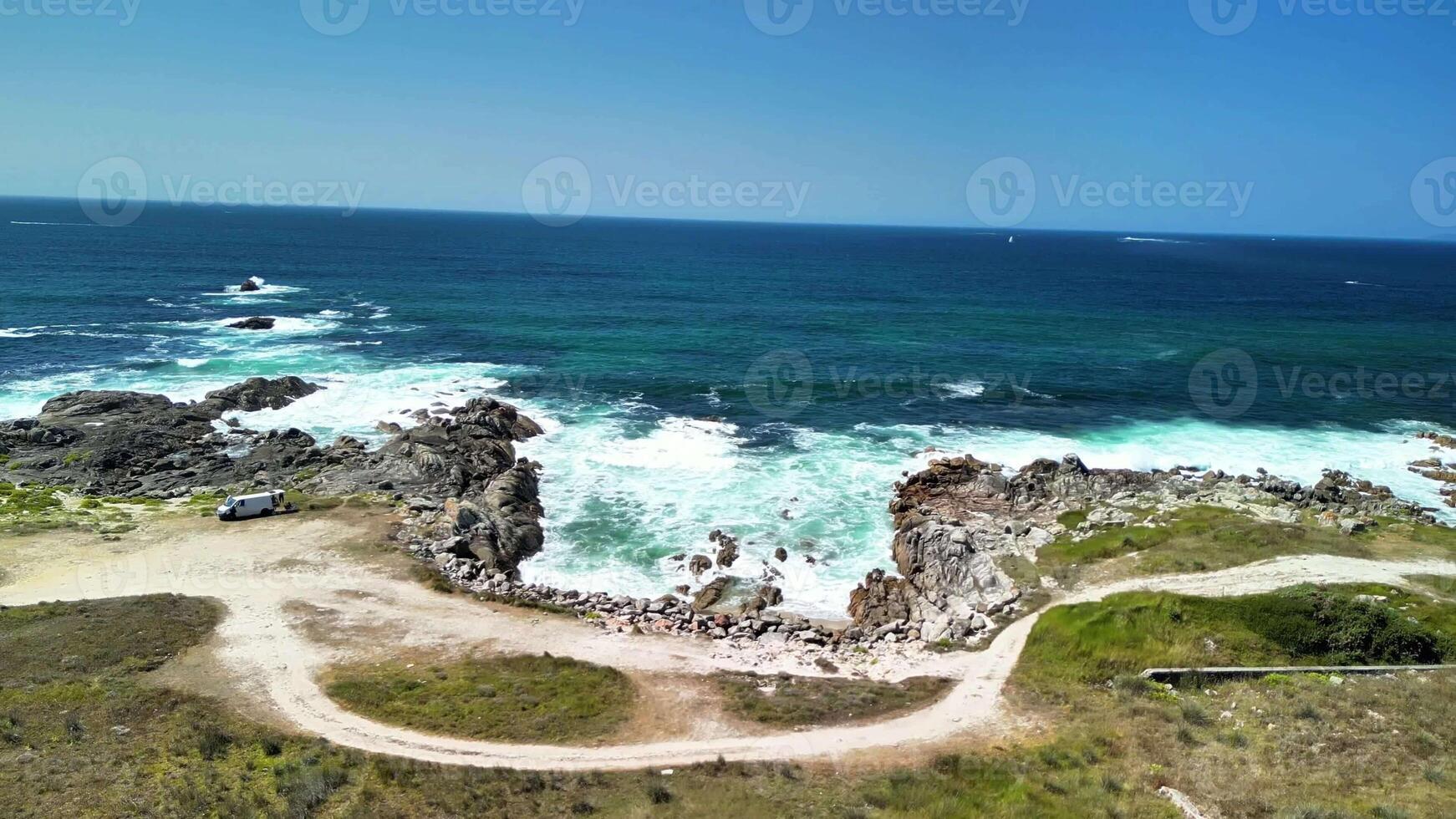 Experience stunning coastal views with roaring waves, rocky formations, and lush greenery under a clear blue sky photo