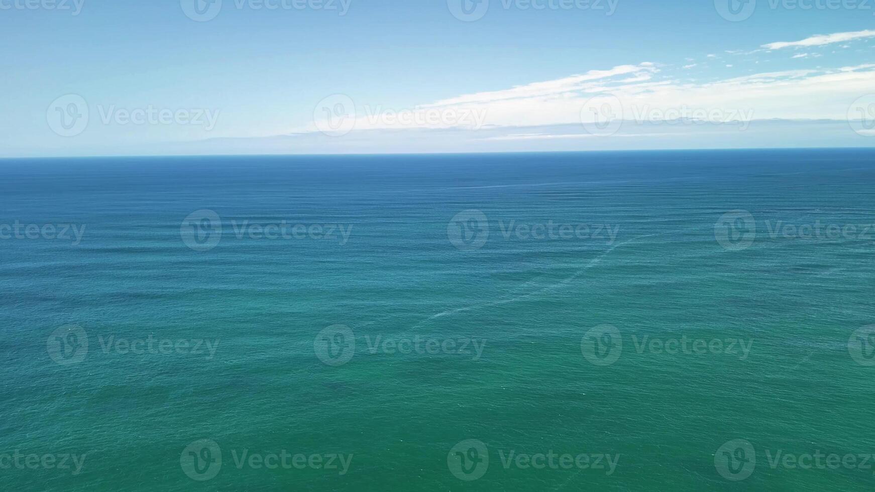 A breathtaking aerial view showcases the calm, serene ocean waters with gentle waves beneath a clear, bright blue sky photo