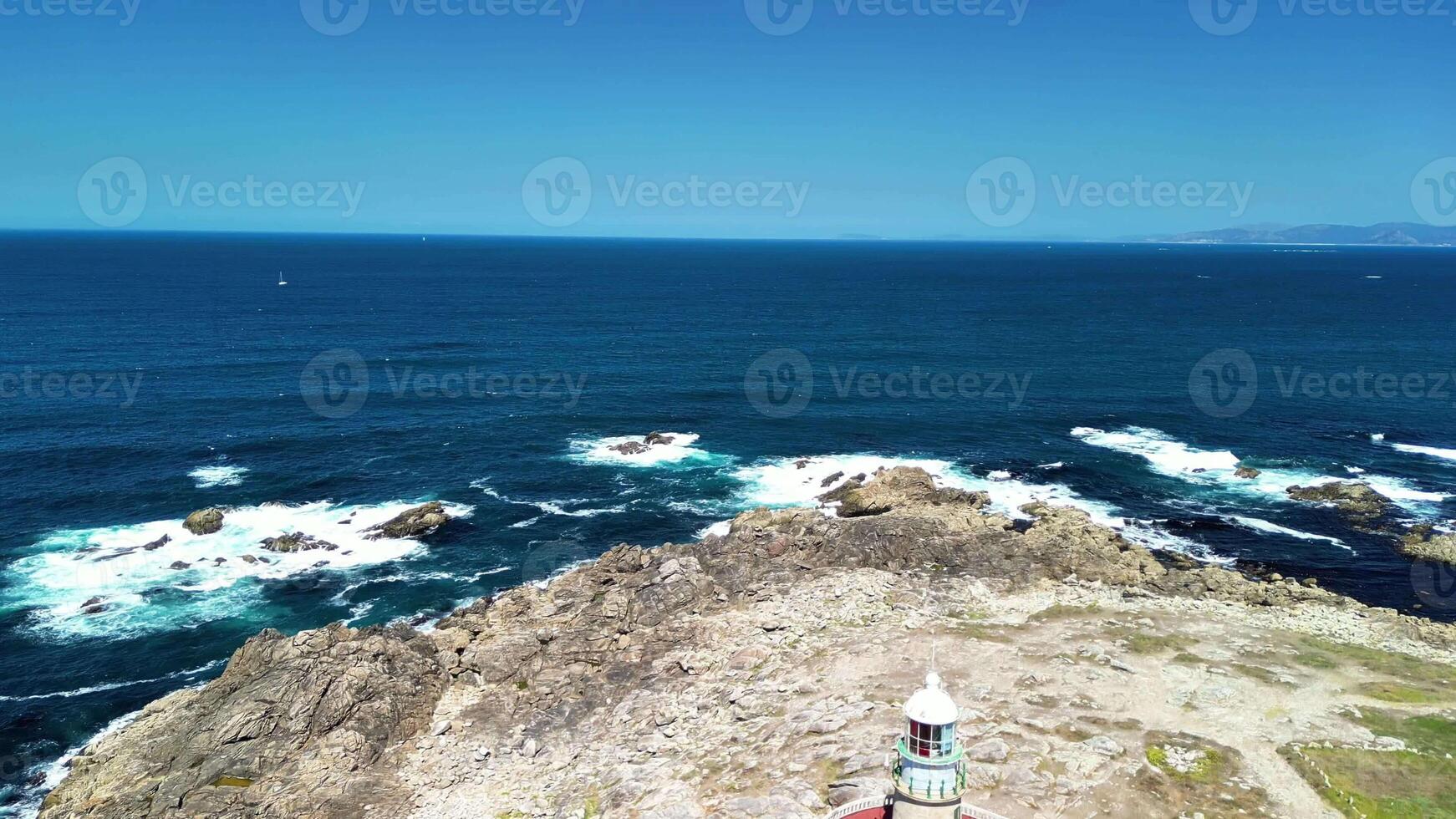 A breathtaking view of the vast ocean with crashing waves, a rugged rocky coastline, and clear blue skies above photo