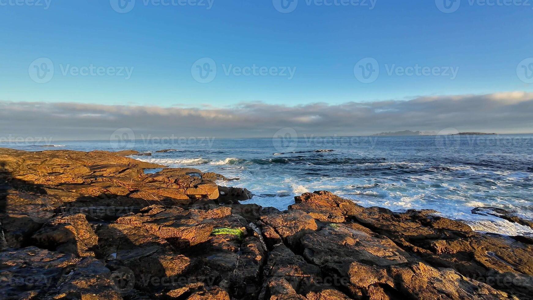 A beautifully tranquil seaside view featuring rugged, majestic rocks and gentle waves under a clear blue sky photo