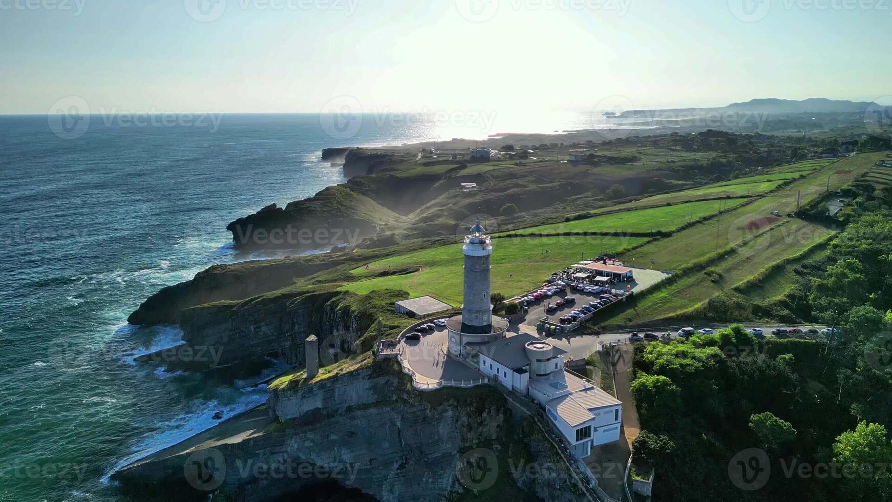 Explore a stunning coastal lighthouse, surrounded by greenery and waves crashing against the cliffs photo