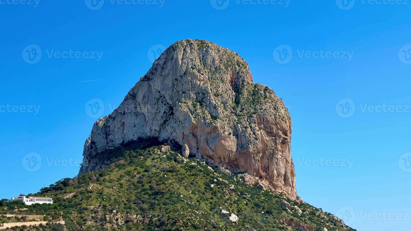 A breathtaking view of an enormous rock formation gracefully surrounded by lush, vibrant greenery and clear blue skies photo