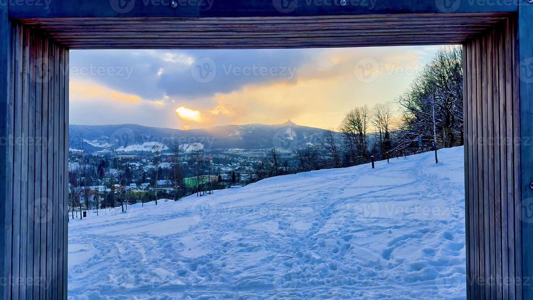 A breathtaking and stunning view of a snowy winter landscape beautifully framed by rustic wood during sunset photo