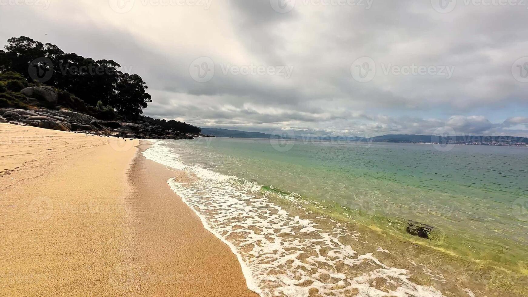 This serene beach scene showcases the soft sands and perfectly calm waters, all beneath a cloudy, overcast sky photo
