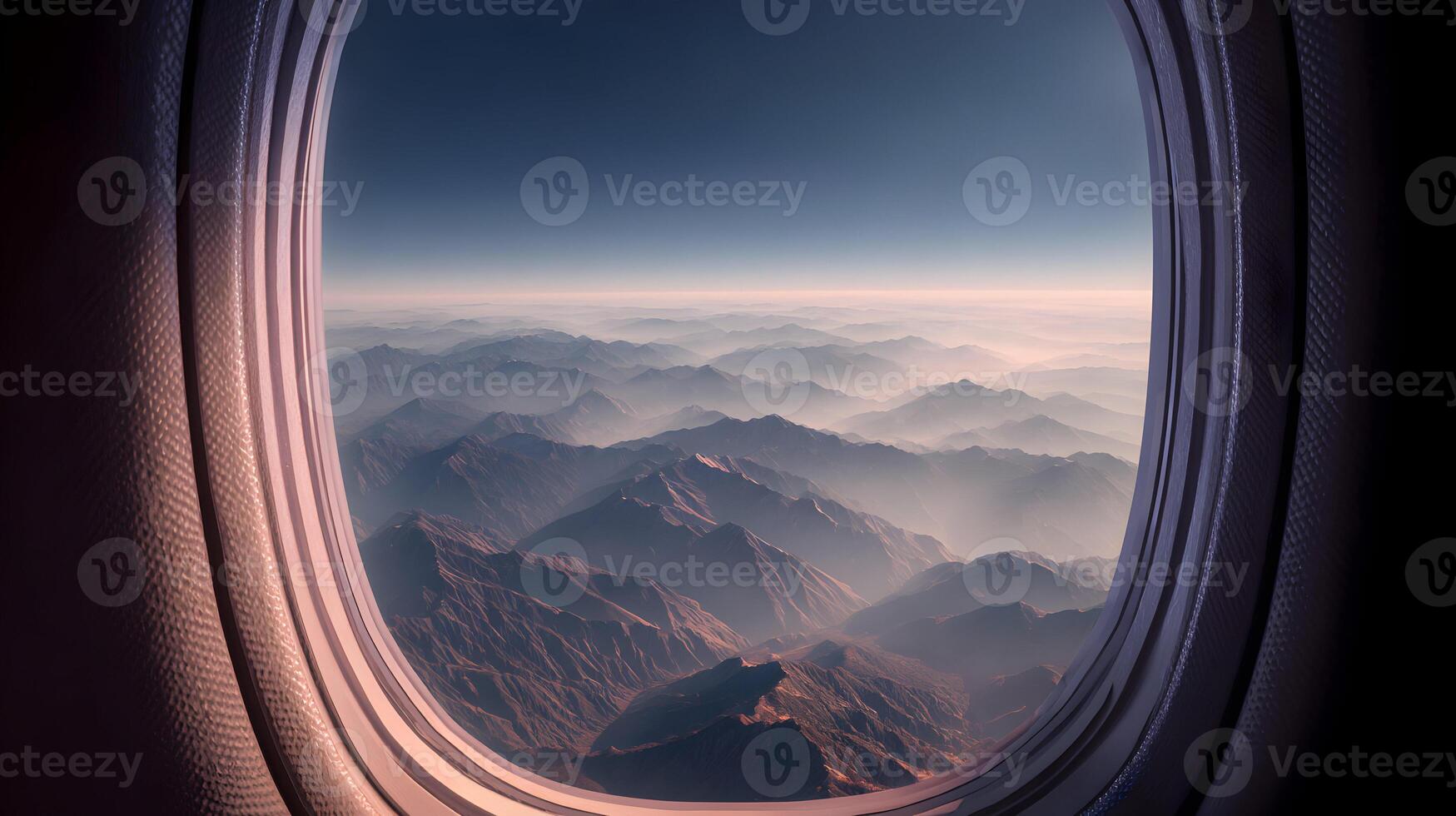 Aerial vista from aircraft cabin captures majestic mountain range shrouded in soft mist and serene blue sky photo