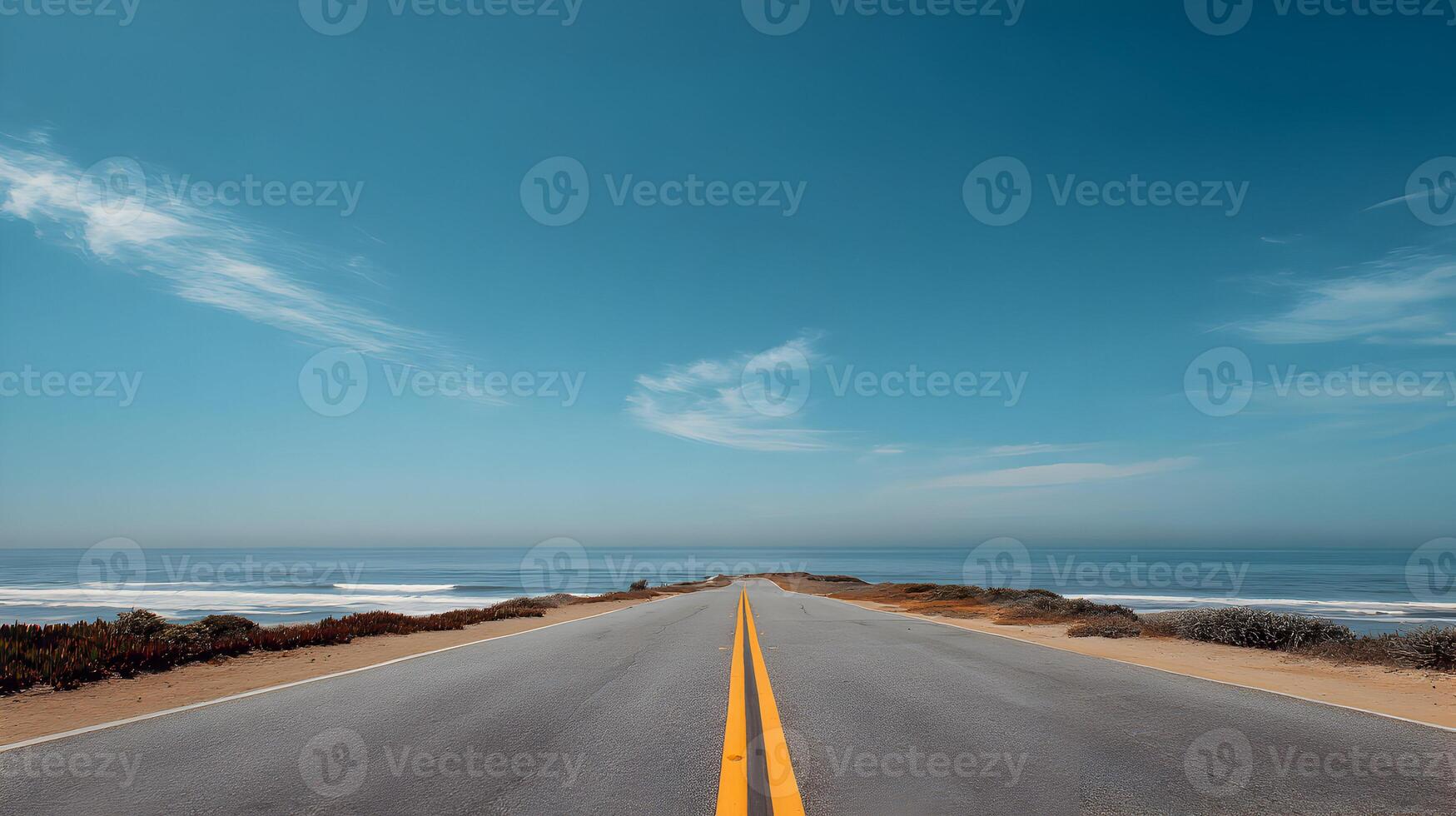 A scenic road leads towards the horizon where the ocean meets the sky on a clear tranquil day photo