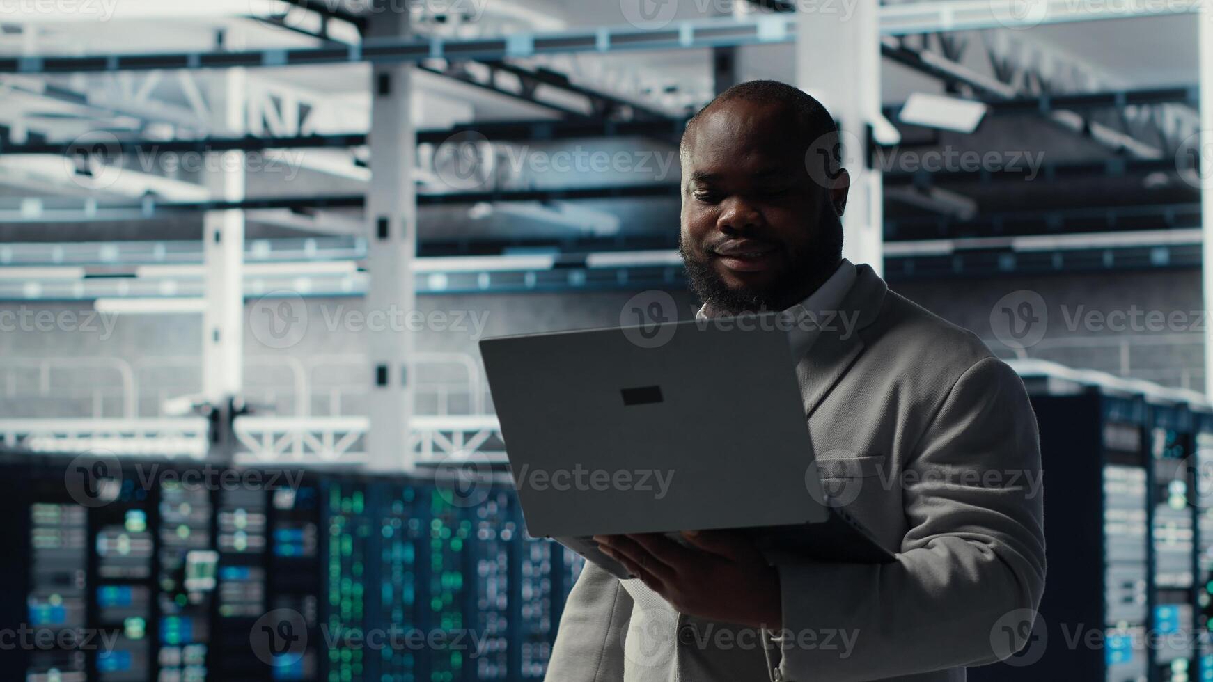 Server room worker auditing systems for vulnerabilities using software on laptop. Engineer walking in data center doing backups and recovery protocols using notebook, camera B photo