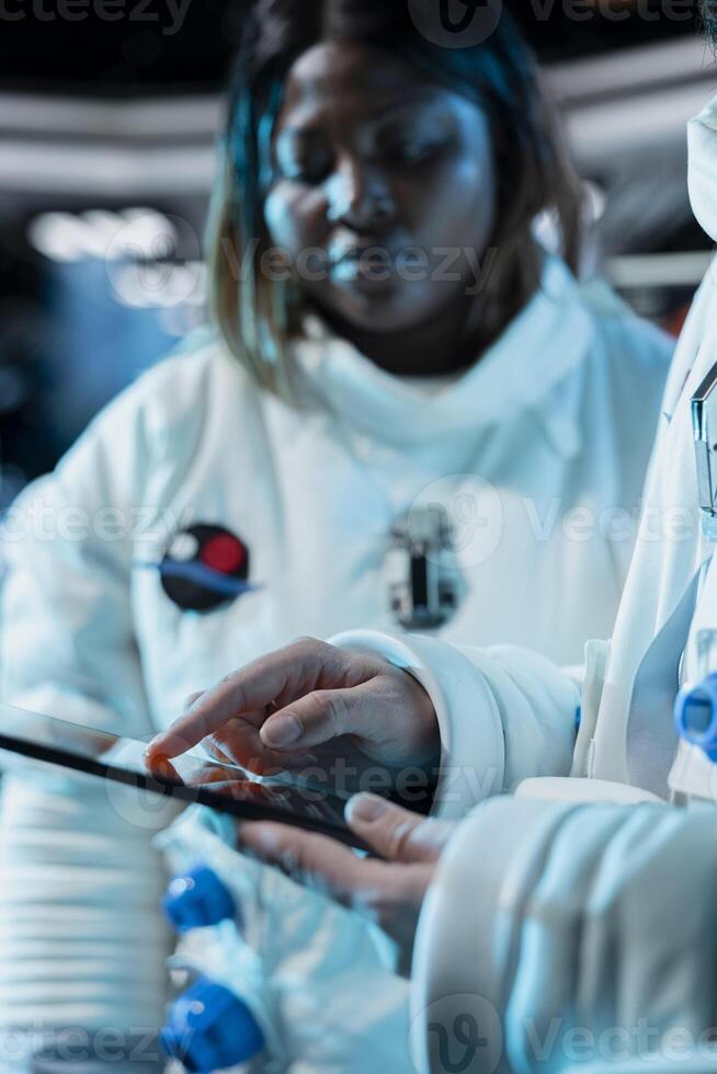 Close up of female astronaut scientist tracking star and asteroids patterns using tablet, recording findings. Researcher wearing cosmonaut gear in spaceship doing research, looking at galaxy visualization photo
