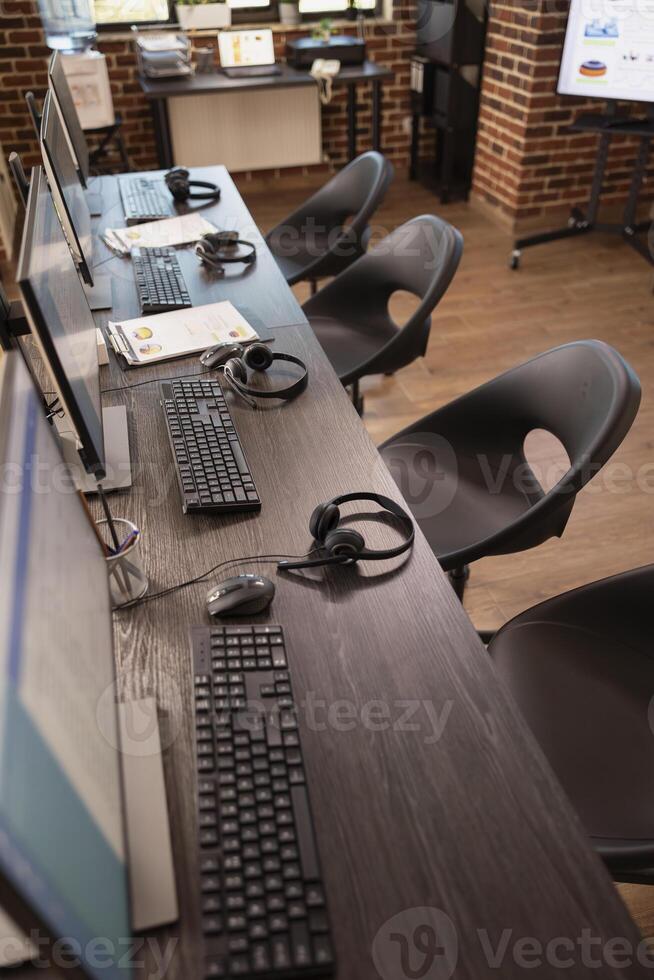 Vacant collaboration space in modern office, featuring multiple desks, digital monitors and headsets, ideal for customer support team. Empty table neatly organized with devices for group of employees. photo