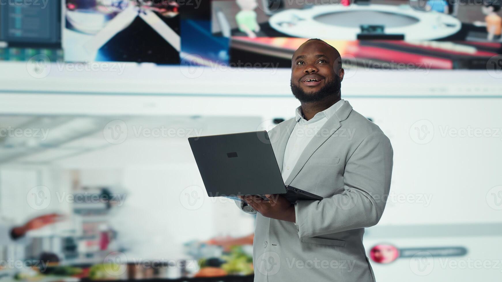 Smiling person uses laptop, enjoying leisure time with content on streaming services. Joyful man watches media VOD broadcasts on notebook in front of digital backdrop filled with clips, camera A photo