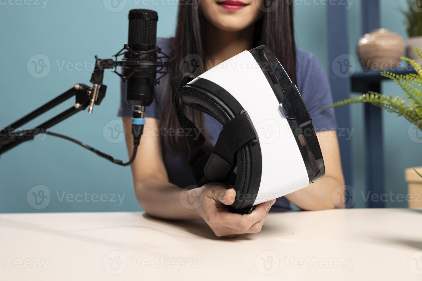 Closeup of social media influencer holding virtual reality goggles, speaking into a mic during a live broadcast. She is reviewing VR headset for an online audience, showcasing the product in detail. photo