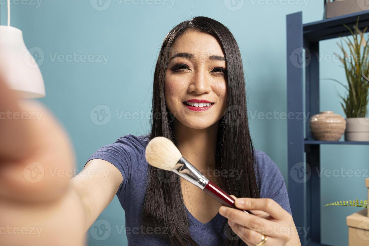 Fashion blogger recording a livestream tutorial, presenting makeup tools and engaging her viewers. She shares insights into cosmetic brushes and makeup techniques for her audience. photo
