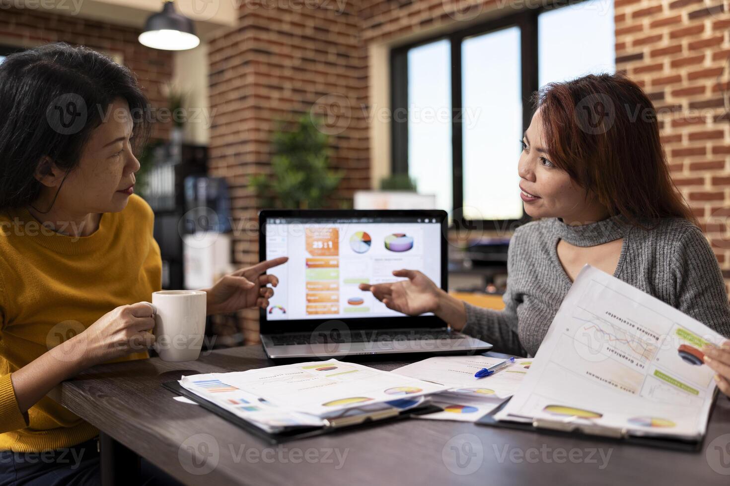 Financial expert advising an investor on market trends, examining the charts on laptop. Business female analysts collaborate on financial reports, reviewing company analytics data on device screen. photo