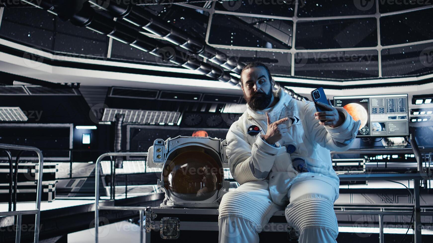 Astronaut doing hand gestures while taking selfies with smartphone inside space station during exploration mission. Man takes pictures with mobile phone during cosmic expedition photo