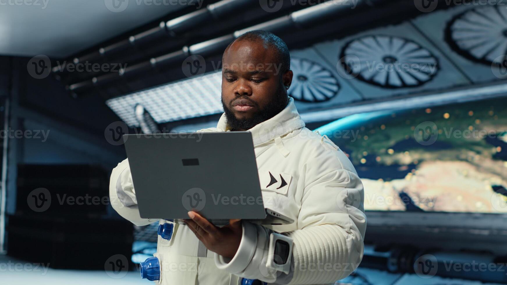 Astronaut in spacecraft using laptop to run telemetry data analysis. Man in spaceship wearing spacesuit analyzing mission logs on notebook during planetary exploration, camera B photo