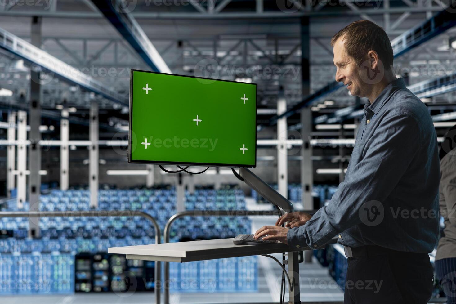 Cheerful IT server room expert uses chroma key computer to minimize hardware downtime. for increased storage capacity. Jolly data center engineer using green screen PC to automate anomaly detection photo