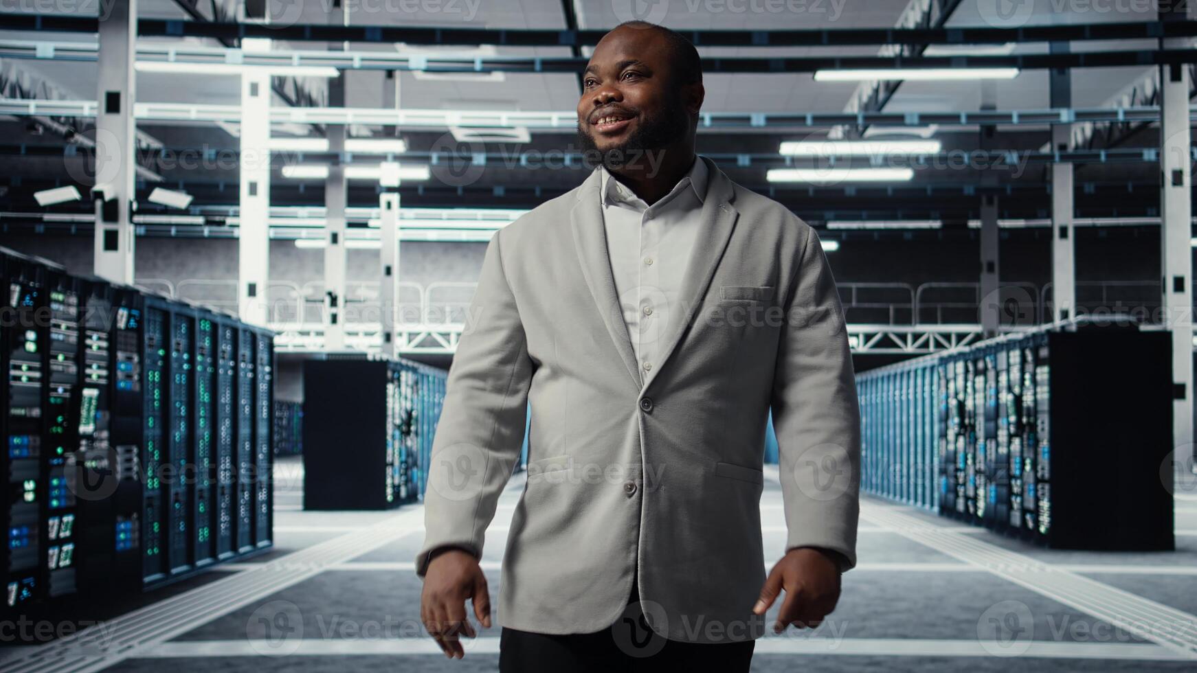 Smiling employee walking in high tech data center with machines powering networks, running companies databases. Admin overseeing server farm with rigs modules processing large datasets, camera A photo