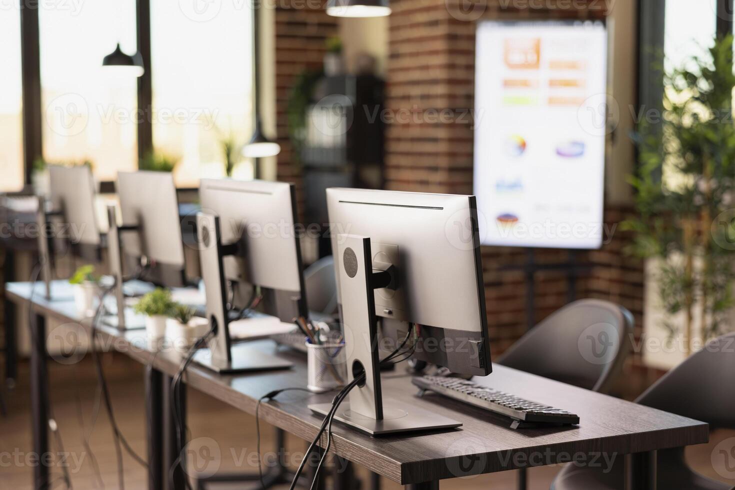 Vacant and organized brick wall office featuring a table and digital equipment for startup company. Empty modern workspace that is well arranged with multiple computers, ready for employees. photo