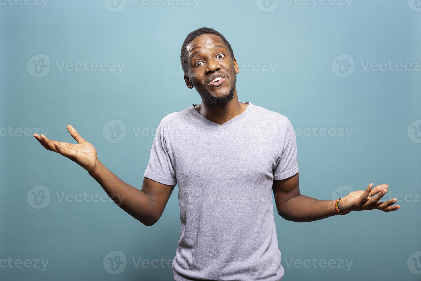 Young black man doing I dont know gesture in a studio, raising shoulders and expressing indecision. African american guy standing with open arms, shrugging in confusion against an isolated background. photo