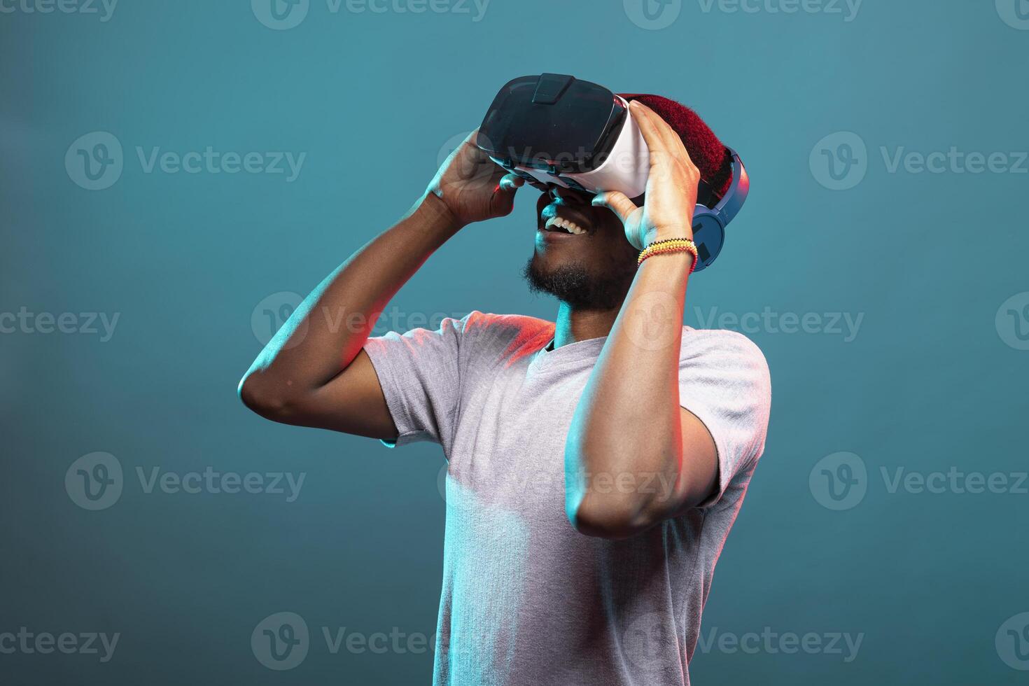 Black male model playing an interactive VR game, engaged in a futuristic 3D simulation, adjusting his headset. African american man looking upward and exploring a virtual reality world. photo
