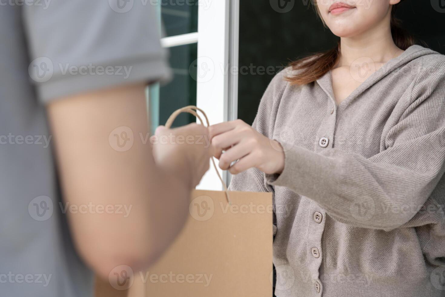 Happy smiling Asian woman receives paper bag parcel of food from courier front house. Delivery man send deliver express. online shopping, paper container, takeaway, postman, delivery service, package. photo