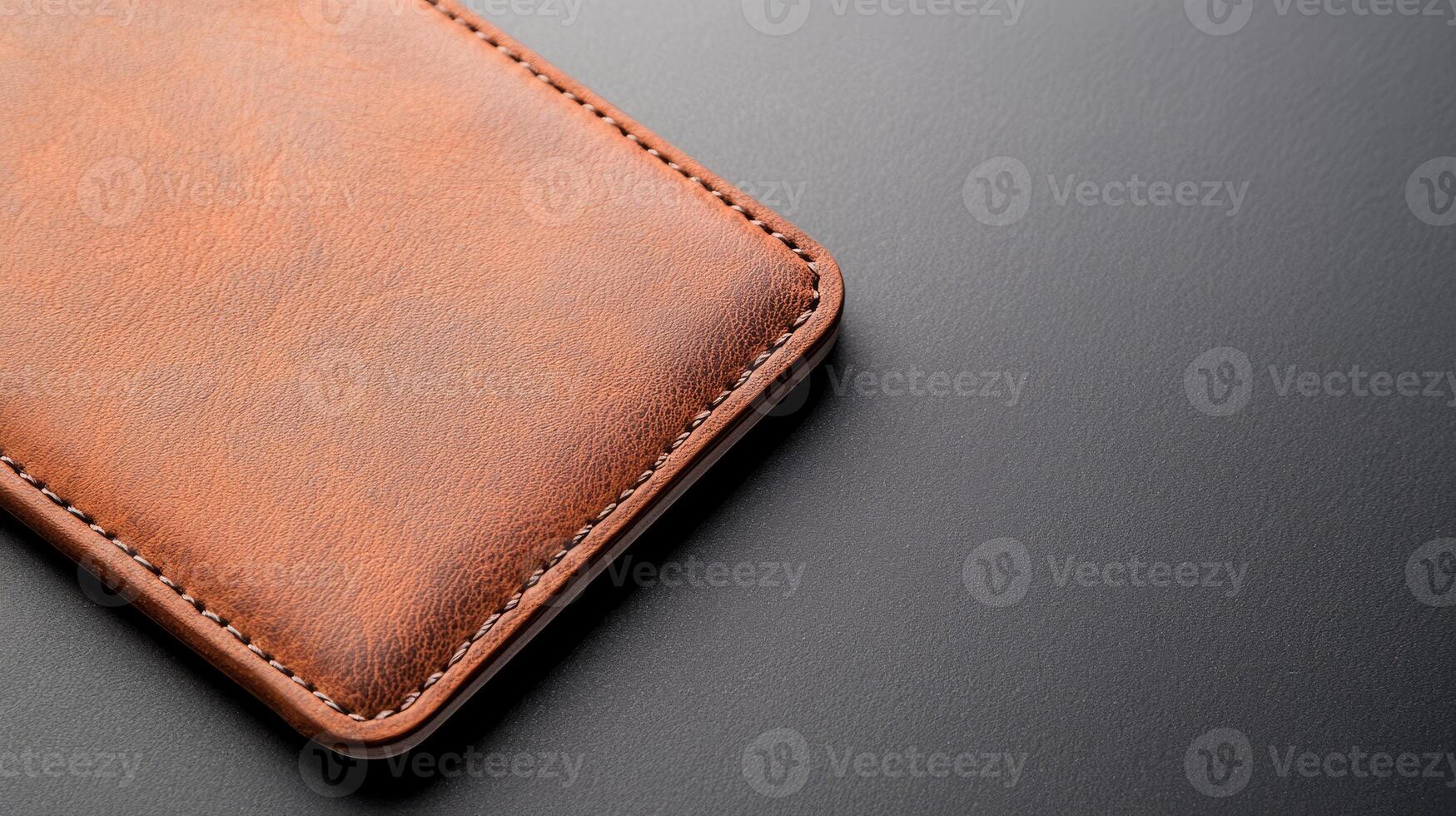 A brown leather phone case rests atop a sleek dark surface, showcasing its quality design and craftsmanship with fine stitching details photo
