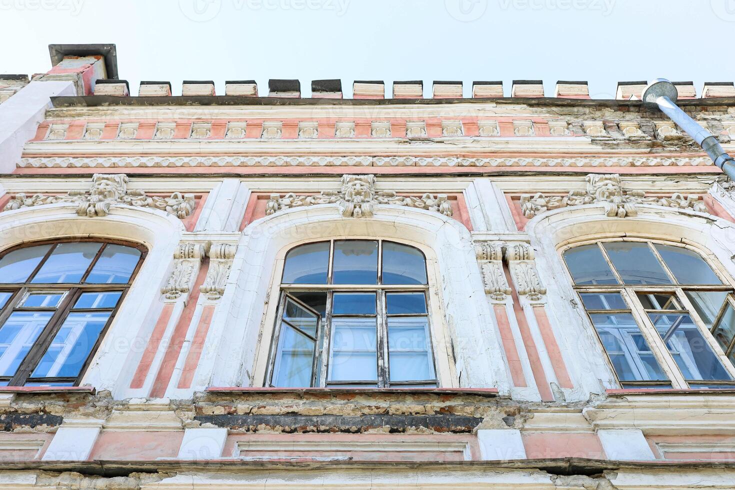 Bottom view to architectural detail of historic building with ornate windows and weathered facade photo