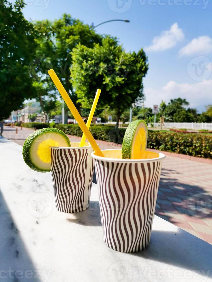 Refreshing beverage cups with lemon and lime garnishes in a sunny outdoor setting photo
